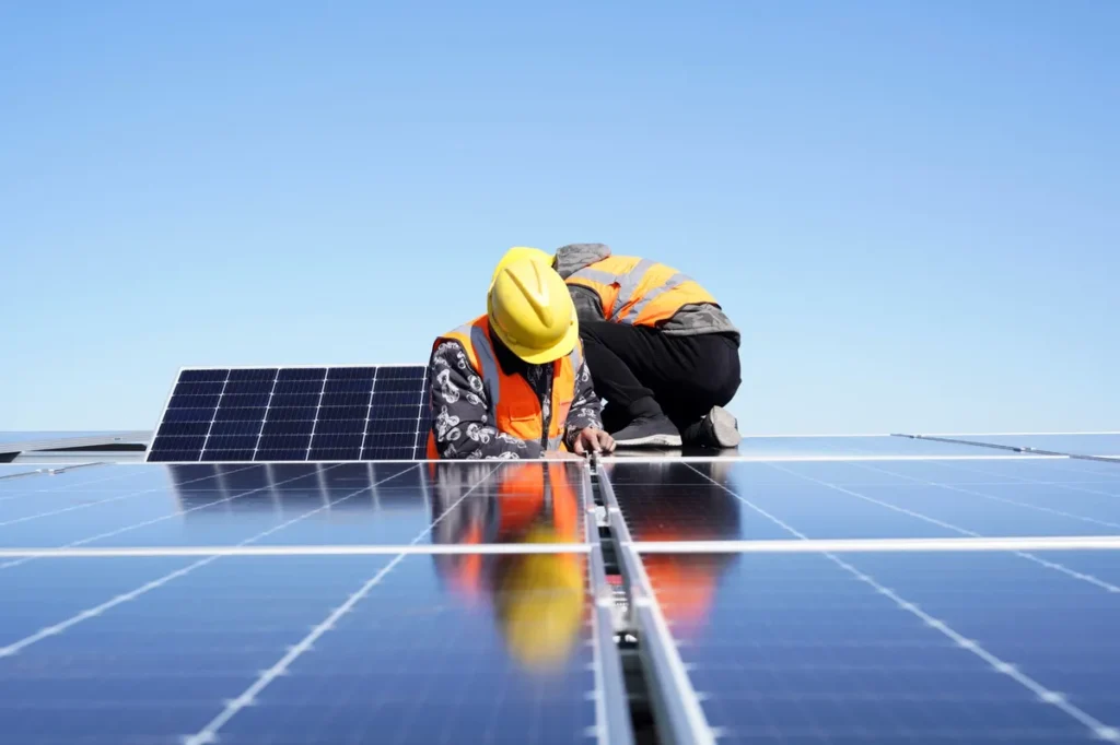 Deux installateurs de panneaux solaires travaillant sur un toit sous un ciel dégagé.